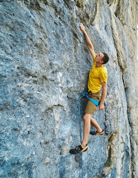 Grimpeur au maillot jaune et baudrier bleu sur une paroi verticale de couleur légèrement bleue